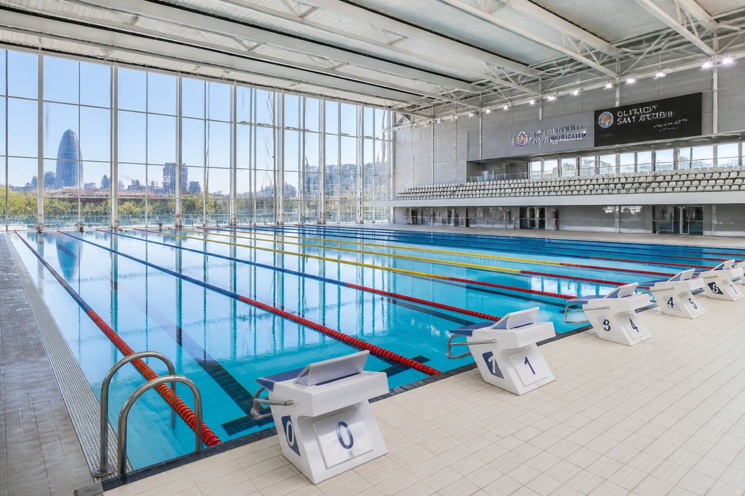 Indoor Olympic-size swimming pool with glass walls and clear water inside a sports complex.