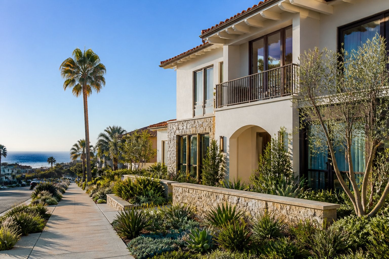 An upscale Santa Monica home with a landscaped garden, palm trees, and the Pacific coastline in the background.