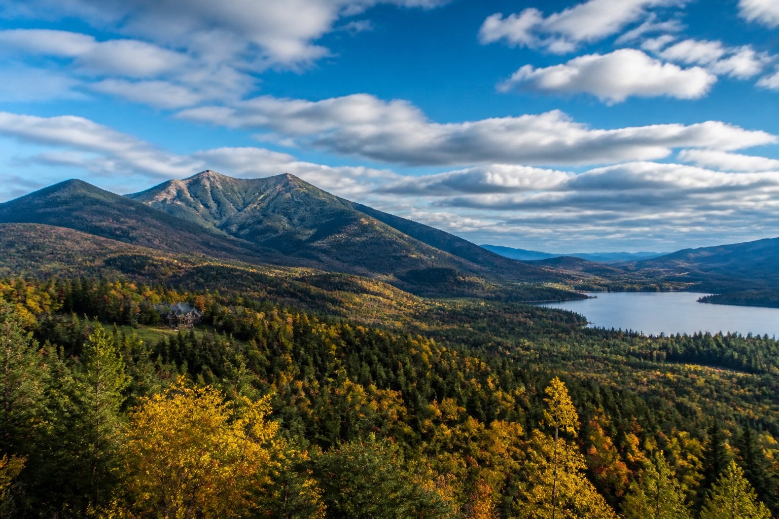 Whiteface Mountain rising above forested Adirondack valleys with a distant lake and scattered mountain lodges.