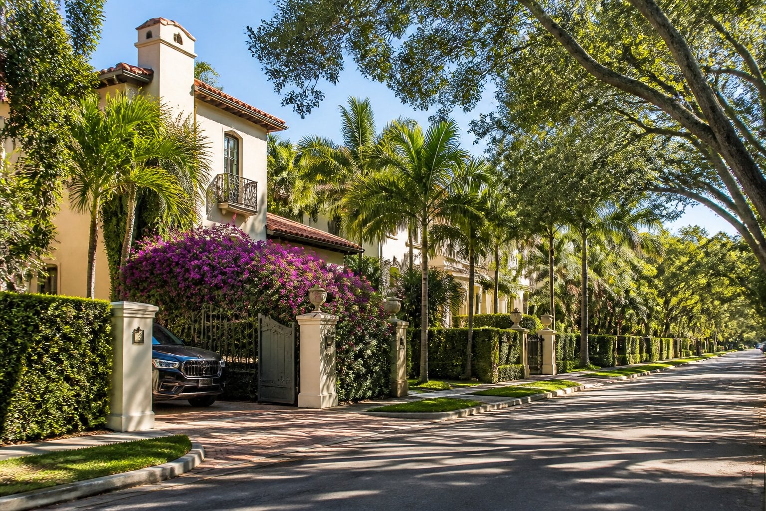 A tree-lined Coral Gables street with elegant Mediterranean-style homes, tropical landscaping, and manicured lawns.