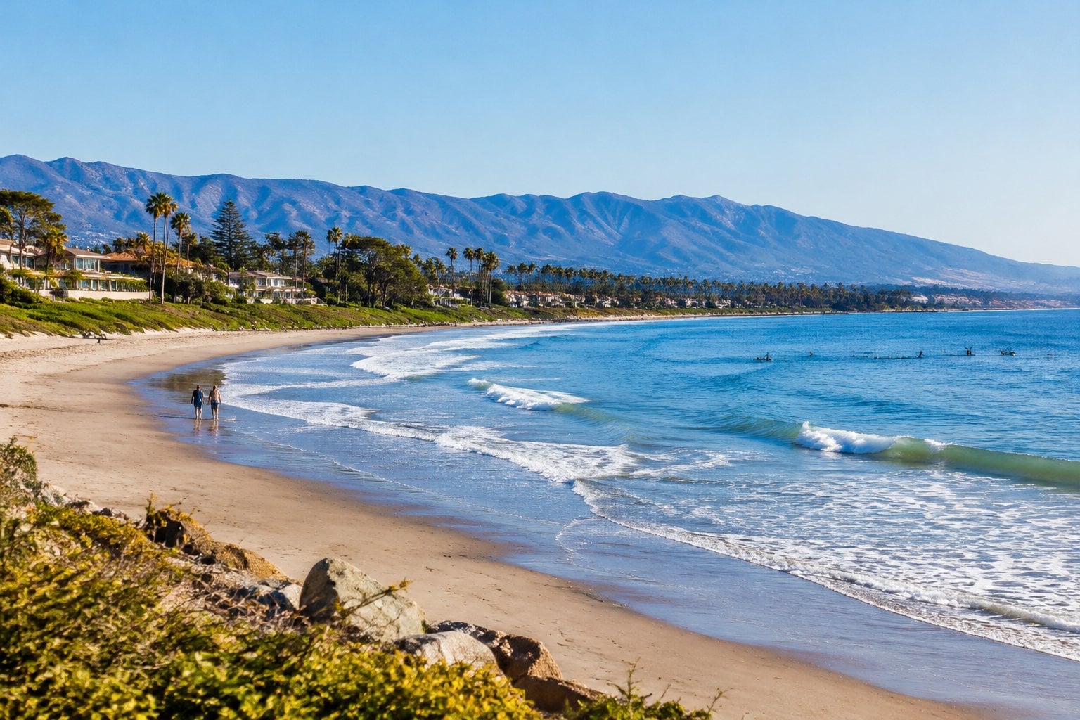 People stroll along a sandy Carpinteria beach beside gentle Pacific waves.